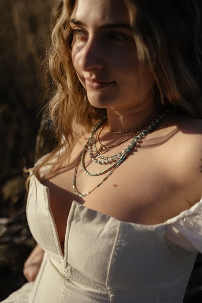 Layered handmade beaded and gold necklaces worn in warm golden-hour light